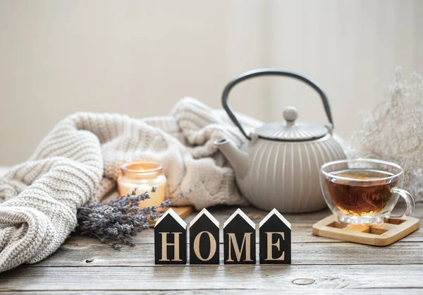 Çaydanlık ve ahşap bir yüzey üzerinde çay ile sakin bir hayat örgü ögesi, samimi detaylar ve bulanık bir arka planda dekoratif bir kelime olan ev..