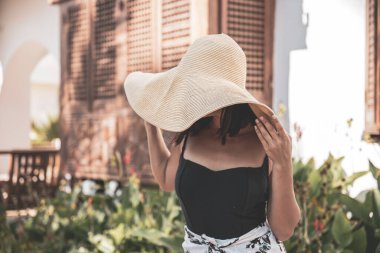 Sıcak bir yaz gününde, eski bir evin cephesinde büyük hasır şapkalı bir kız..