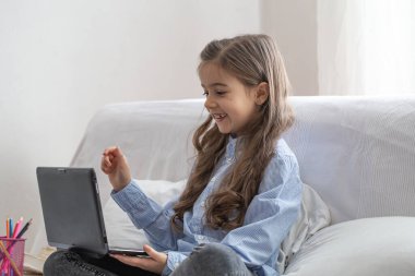 Koronavirüs salgını nedeniyle karantina sırasında internetten alınan bir derste evde dizüstü bilgisayarla oturan bir ilkokul öğrencisi..