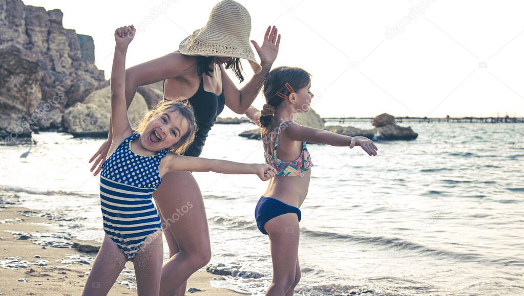 A young mother and two little daughters are having fun, dancing and laughing on the seashore. Happy family on vacation.