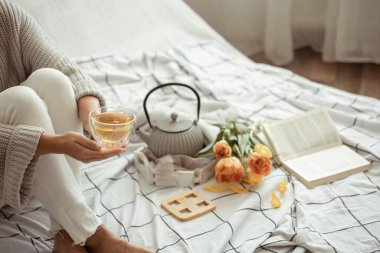 Bir fincan çay, çaydanlık, bir buket lale ve yatakta bir kitapla sakin bir hayat. Hafta sonu ve bahar sabahı kavramı.