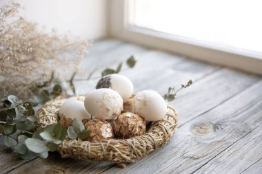 Paskalya, süslü Paskalya yumurtaları ve kuru dallarla dolu tahta bir yüzey üzerindeki dekoratif yuvalarla dolu..