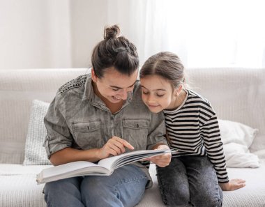Neşeli anne ve kızı evde dinleniyor, birlikte kitap okuyorlar. Mutlu aile ve dostça ilişkiler kavramı..