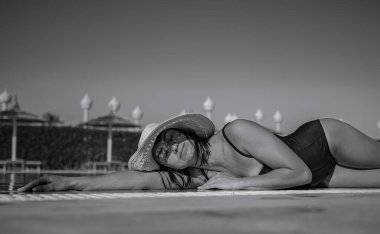 Çekici bir kız hasır şapka ve mayo giyerek güneşte dinleniyor. Sıcak bir ülkede tatil kavramı. Siyah beyaz fotoğraf.