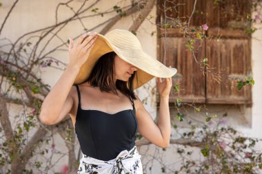 Genç bir kadın, büyüyen bir ağacın kurumuş dallarıyla çevrili bir duvarın yakınındaki büyük bir hasır şapkanın altında güneşten saklanıyor..