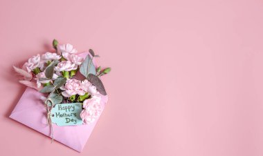 İçinde taze çiçekler olan bir zarf ve Anneler Günün kutlu olsun yazan şenlikli bir kompozisyon..