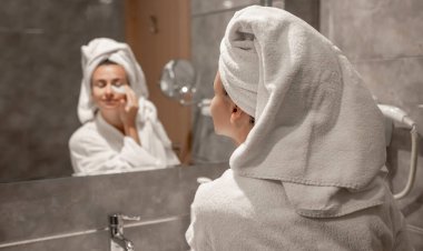 Kafasında havluyla bornoz olan bir kız banyoda aynanın önünde gözlerinin altına yamalar yapıştırıyor..