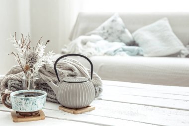 Bir çaydanlık ve içinde dekorasyon detayları olan seramik bir kupa Hygge tarzı oturma odasında. Ev konforu ve modern tarz kavramı.