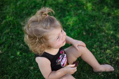 Yazın küçük komik kız bahçedeki çimenlerde oturur elinde bir parça çikolatayla..