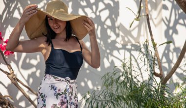 Kıvırcık, yaşlı bir ağaçla kaplı bir duvarın önünde büyük hasır şapkalı bir kız..