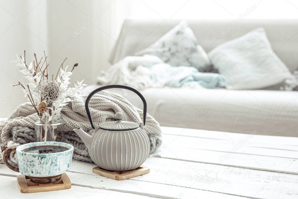 A teapot and a beautiful ceramic cup with decor details in a hygge style living room. The concept of home comfort and modern style.