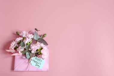 İçinde taze çiçekler olan bir zarf ve Anneler Günün kutlu olsun yazan şenlikli bir kompozisyon..