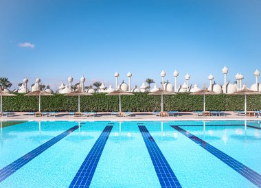 Güneşli plaj, temiz suyla birlikte havuz kenarında saman şemsiyeler. Mısır 'da tatil yeri.