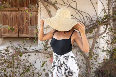 Genç bir kadın, büyüyen bir ağacın kurumuş dallarıyla çevrili bir duvarın yakınındaki büyük bir hasır şapkanın altında güneşten saklanıyor..