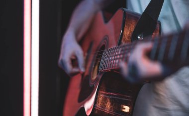 Bir adam karanlık bir odada akustik gitar çalar. Canlı performans, akustik konser.