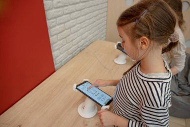 Alet dükkanındaki küçük bir kız telefonu inceliyor. Bir çocuk için yeni bir akıllı telefon seçmek.