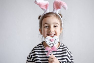 Çubuğun üzerinde Paskalya zencefilli ekmeği ve kafasında dekoratif tavşan kulakları olan sevimli küçük bir kız..