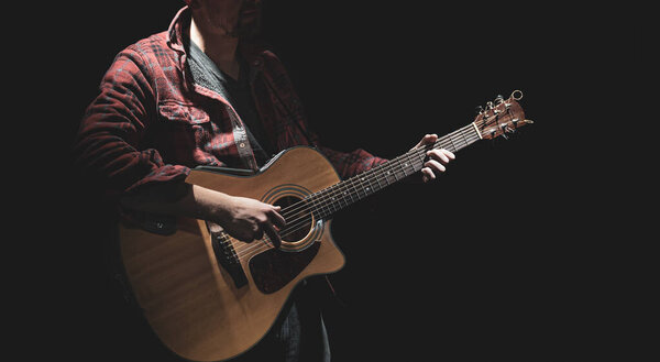 Male guitarist playing acoustic guitar in dark room.