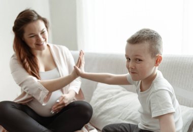 Küçük çocuk evde kanepede oturan hamile anneye beşlik çakıyor..