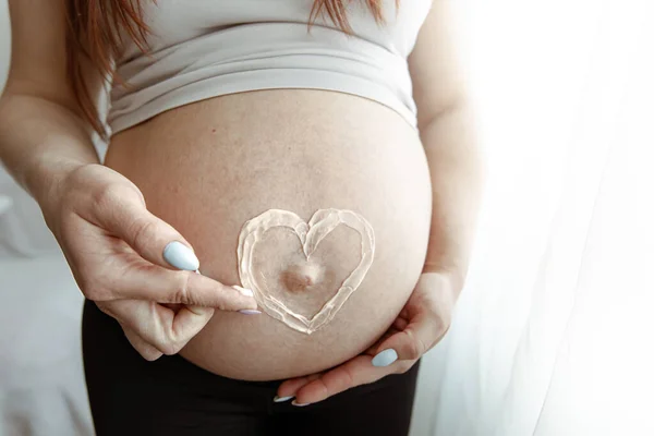 在怀孕的最后几个月里 用粉刷过的心脏膏对未来母亲的裸体腹部进行了近距离观察 — 图库照片