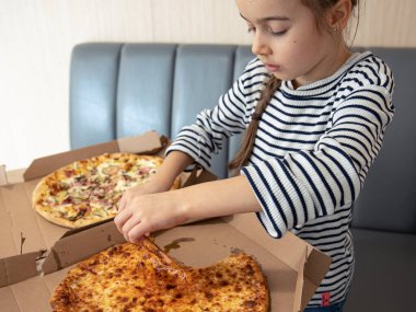 Küçük bir kız öğle yemeğinde pizza yer ve en iyi parçayı seçer..