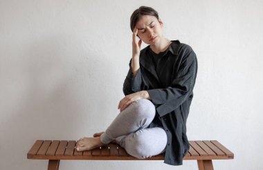 Siyah gömlekli bir kız bankta oturuyor ve zihinsel ya da fiziksel acı çekiyor..