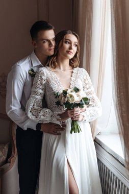 Damat, geline hoş, dantelli bir elbise ve bir buket taze çiçekle nazikçe sarılır. Stüdyoda düğün fotoğrafı çekimi..