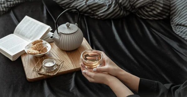 A woman has breakfast in bed with tea and cookies, lying in bed on a day off.