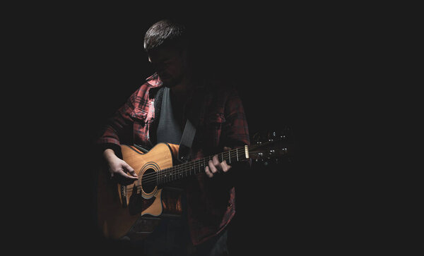 Male guitarist playing acoustic guitar in dark room.