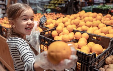 Markette komik küçük bir kız portakal seçiyor..