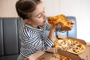 Küçük kız öğle yemeğinde iştah açıcı peynirli pizza yiyor. Lezzetli peynirli pizza..