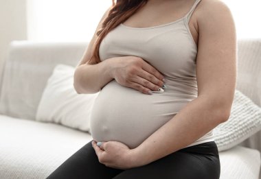 Hamile bir annenin karnını kapat. Evdeki kanepede otur..