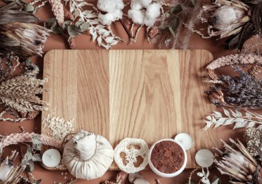 Kurumuş kır çiçekleri ve gövde bakım ürünleri ile merkezdeki ahşap bir element üzerinde kompozisyon.