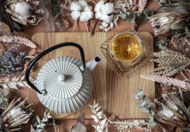 Kuru kır çiçekleri ve bir çaydanlık içindeki doğal bitki çayıyla ahşap bir yüzey üzerinde kompozisyon.