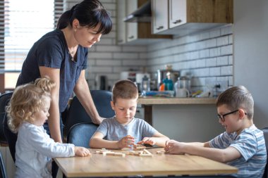 Küçük çocuklar anneleriyle mutfakta tahta küplerle masa oyunu oynuyorlar..