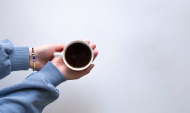 Kapalı bir fincan koyu kahve, beyaz manzarada izole edilmiş kadın ellerinde..