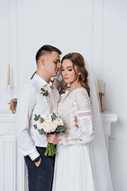 Damat sıcak bir odada, boho tarzı dantel bir gelinlik içinde geline sarılıyor. Stüdyoda düğün fotoğrafı çekimi..