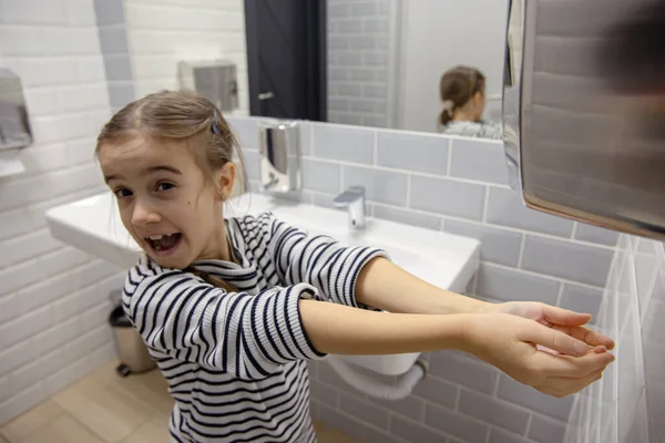 Funny little girl dries her hands in the bathroom. Hygiene and cleanliness in a coronavirus environment.