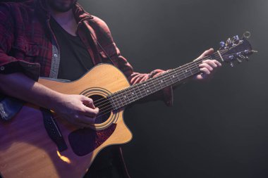 Erkek müzisyen karanlık bir odada akustik gitar çalıyor..