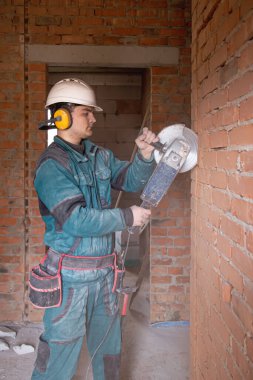 Bir iş tesisinde koruyucu miğfer takmış elektrikçi inşaat işçisi bir öğütücüyle çalışıyor..