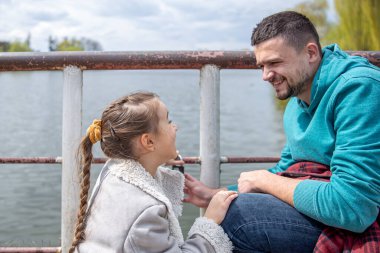 Küçük kız ve baba parkta yürürken birbirlerinin gözlerinin içine bakarak eğleniyorlar..