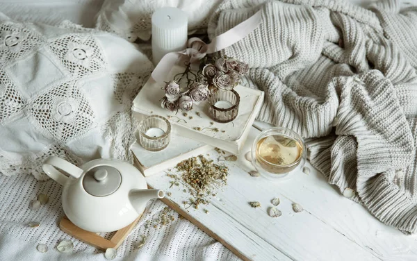 Cozy light still life with candles, tea, teapot and flowers as decor.