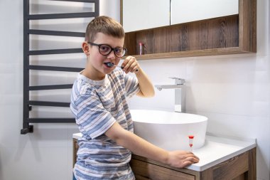 Küçük şirin bir çocuk dişlerini fırçalıyor ve saati kum saatiyle tutuyor..