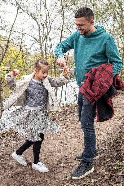 A little girl is a whirl, holding her dad's hand for a walk in the woods.