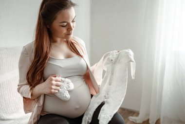 Hamileliğinin son aylarında hamile kalan anne ellerinde bebek kıyafetleri ve botlarıyla..