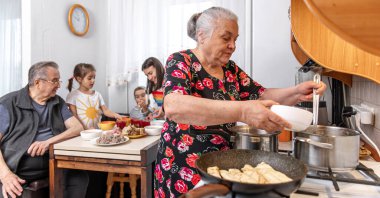 Sobanın başında yaşlı bir kadın öğle yemeği için aileye çorba dolduruyor..