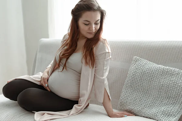 一个年轻的孕妇躺在一间明亮舒适的房间里的沙发上 — 图库照片