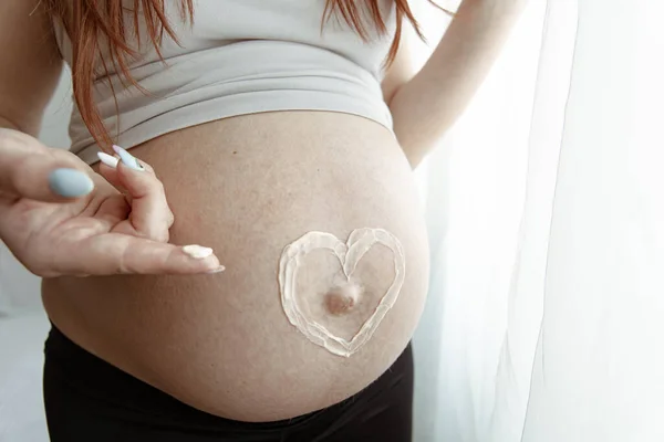 在怀孕的最后几个月里 用粉刷过的心脏膏对未来母亲的裸体腹部进行了近距离观察 — 图库照片