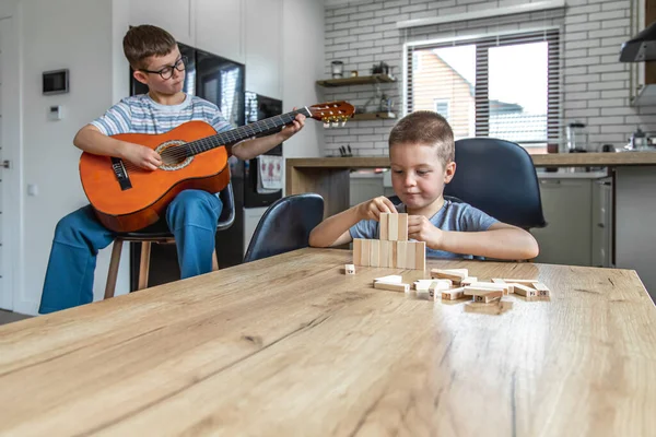 Niño Toca Guitarra Hermano Construye Una Torreta Con Cubos Madera — Foto de Stock