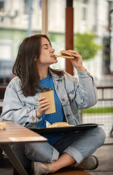 Chica Atractiva Estilo Casual Come Una Hamburguesa Con Café Sentado — Foto de Stock